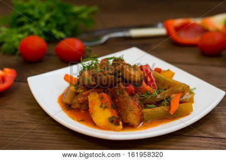 Stew with potatoes, carrots, pickles, tomatoes and hot peppers. Azu by Tartarian on a white square plate. Wooden rustic background. Top view