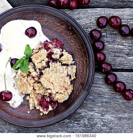 Homemade Cherry crumble wiht ice cream and cherries on an old wooden table background.Selective focus.