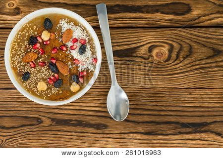 Bowl With Delicious Sweet Brown Asure Dessert And Assorted Nuts Sprinkled In It On Wooden Grain Tabl