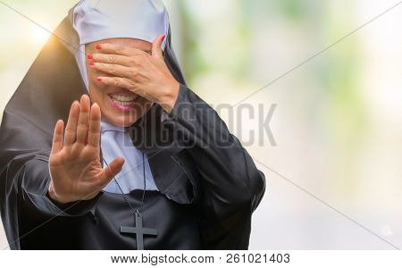 Middle age senior christian catholic nun woman over isolated background covering eyes with hands and doing stop gesture with sad and fear expression. Embarrassed and negative concept.