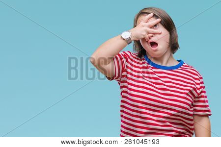 Young adult woman with down syndrome over isolated background peeking in shock covering face and eyes with hand, looking through fingers with embarrassed expression.
