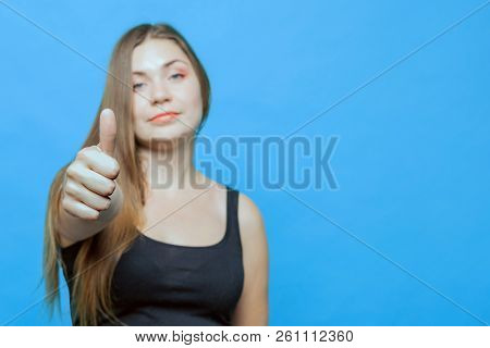 Young Attractive Caucasian Woman Makes Thumb Up, Focus On The Tumb. Blue Eyes. Blue Backgroung, Isol
