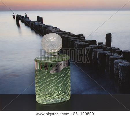 Eau De Rochas, Fragrance For Ladies, Large Perfume Bottle In Front Of The Picture Of A Groyne In The