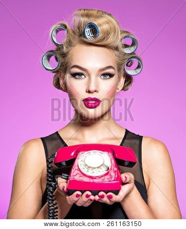 Young girl in curlers holds a retro phone. Young attractive woman with blue culers using an old phone. Girl holding a red  telephone.