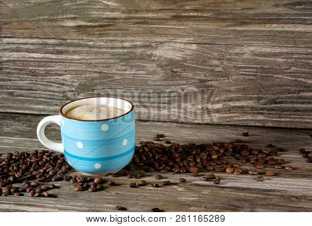 Photo Of A Blue Cup Of Fragrant Coffee On A Background Of Coffee Beans And A Wooden Table
