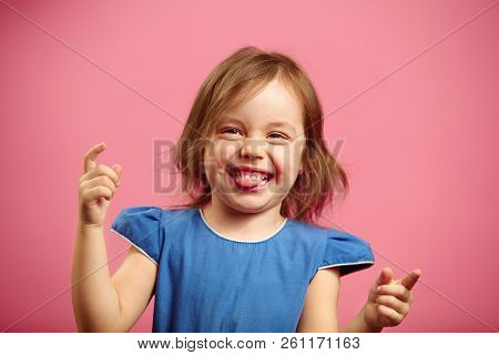 Portrait Of Joyful Little Girl In Good Mood, Bit Her Tongue, Raised Hands Up.