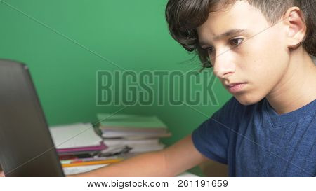 Profile Of A Teenager Boy, On A Green Background. Close-up. The Boy Is Concentrating On The Laptop S