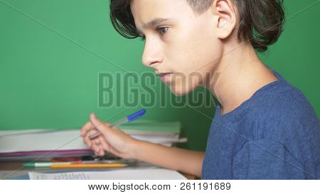 Profile Of A Teenager Boy, On A Green Background. Close-up. The Boy Is Concentrating On The Laptop S
