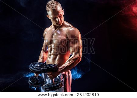 Topless Man Exercising Biceps With Dumbbells Posing In Studio Fuul Of Colored Smoke