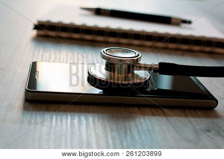 Stethoscope On A Black Smartphone Next To A Notepad And Biro - Fixing A Broken Mobile Phone Concept