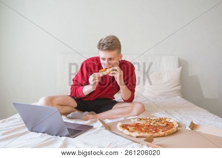 An Attractive Young Man Is Sitting On The Bed In A Cozy Bright Room, Is Focused On Watching A Movie 
