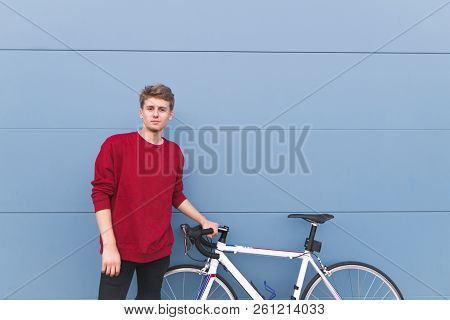 Attractive Young Man In A Red Sweatshirt Stands With A White Blooming On The Background Of A Blue Wa