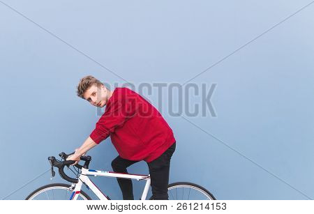 Portrait Of Handsome Man Sitting On White Bicycle On A Background Of Blue Wall And Looking At The Ca