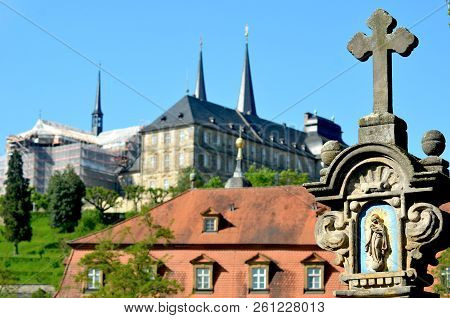 A Stone Shrine Depicts Our Lady And Child. A Cross Is On Top Of The Shrine. In The Background Are So
