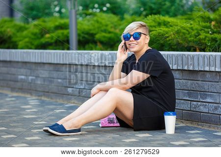 Young Girl Student In Sunglasses Plus Size Sits In The Yard, Sits On Campus Talking On The Phone Wit