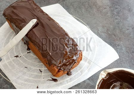 Glazing A Loaf Cake On A Cooling Rack And Parchment Paper With Chocolate Couverture Using A Palette 