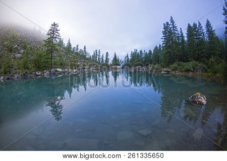 Reflection Of The Shore Of The Lake In The Watery Surface. A Misty Summer Morning. The Large (lower)