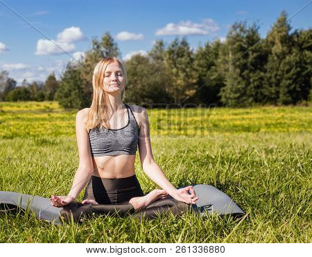 Young Female With Open Arms And Long Blond Hair Relaxes In Yoga Pose In Green Nature