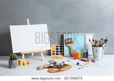 Easel With Space For Design And Set Of Professional Art Supplies On Table Against Grey Background