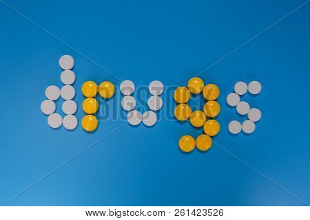 Word Drugs From Color Capsules On The Blue Background. Top View Copy Space Pattern