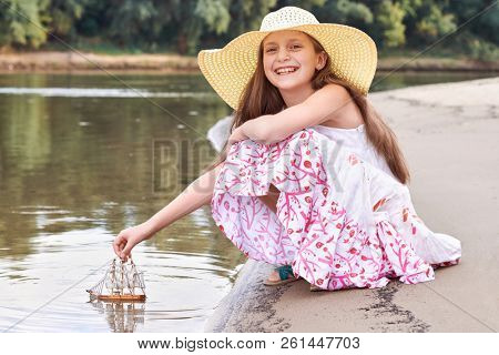 girl playing with a toy sailing ship by the river