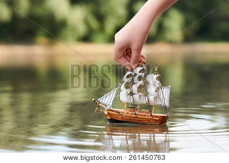 girl playing with a toy sailing ship by the river, hand closeup