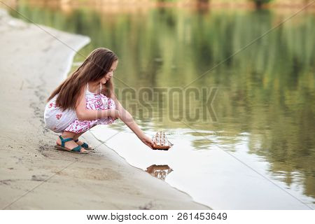 girl playing with a toy sailing ship by the river