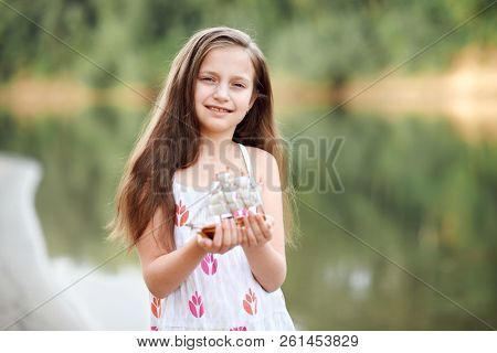 girl playing with a toy sailing ship by the river