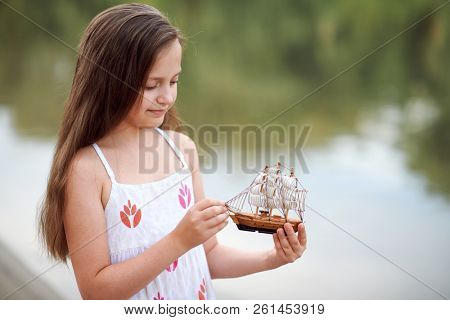 girl playing with a toy sailing ship by the river