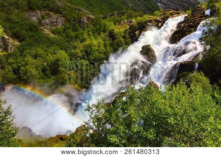 Waterfall And Rainbow On The Way To Briksdal Or Briksdalsbreen Glacier In Olden, Norway And Green Mo
