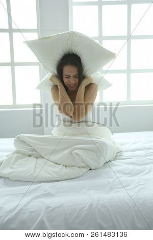 Young caucasian woman covering her head and ears with pillows.