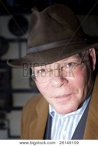 Um contraste rico fecham o retrato de um homem alto, ligeiramente inclinado para a frente, com um chapéu e overc