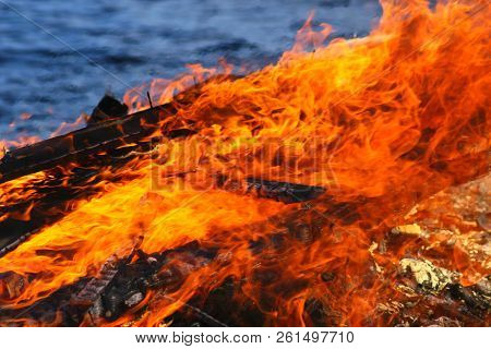 Closeup Of A Large Hot Flames Burning. Water Surface Of A Lake On Blurred Background.