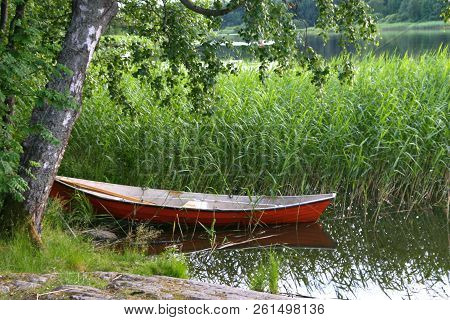 One Red Boat At The Coast Of The Lake. Surrounded With Long Fresh Grown Grass.