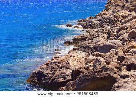 Stones Along The Seashore. Blue Seawater. Small Waves Beating Against The Shore. Unapproachable Dese