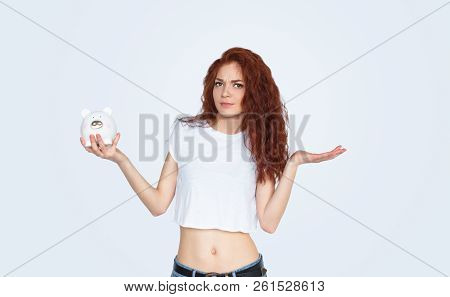 Bewildered Young Woman With Wavy Ginger Hair Holding Piggy Bank And Looking At Camera While Standing