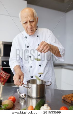 The Aged Chef Cooking A Soup In The Kitchen. The Concepy Of Cooking