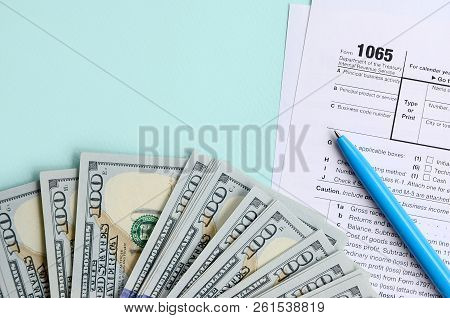 1065 Tax Form Lies Near Hundred Dollar Bills And Blue Pen On A Light Blue Background. Us Return For 