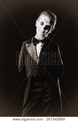Portrait of a child boy with carnival make-up of a skeleton wearing elegant tail-coat. Studio shot over black background. Halloween. Dia de los muertos. The Day of the Dead.