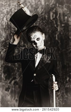 Portrait of a child boy with carnival make-up of a skeleton wearing elegant tail-coat. Studio shot over dark grunge background. Halloween. Dia de los muertos. The Day of the Dead.