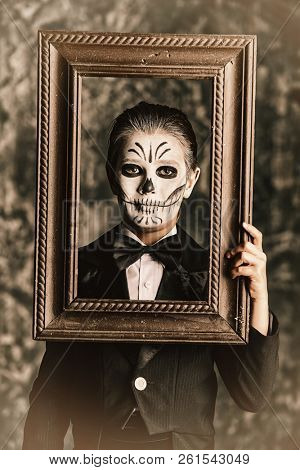 Portrait of a child boy with carnival make-up of a skeleton wearing elegant tail-coat. Studio shot over dark grunge background. Halloween. Dia de los muertos. The Day of the Dead.