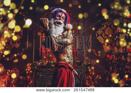 Bad Santa concept. Portrait of a nude tattooed Santa with purple dreads demonstrating antisocial behavior, rudeness and aggression. 