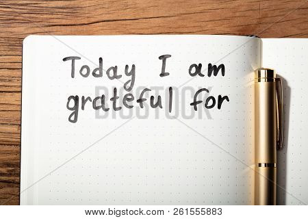 Close-up Of Gratitude Word With Pen On Notebook Over Wooden Desk
