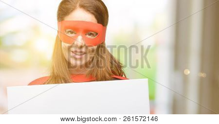 Middle age super hero woman wearing red mask and cape holding blank advertising banner, good poster for ad, offer or announcement, big paper billboard