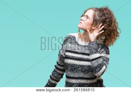 Beautiful brunette curly hair young girl wearing glasses over isolated background smiling with hand over ear listening an hearing to rumor or gossip. Deafness concept.