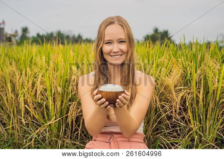 A Woman Is Holding A Cup Of Boiled Rice In A Wooden Cup On The Background Of A Ripe Rice Field