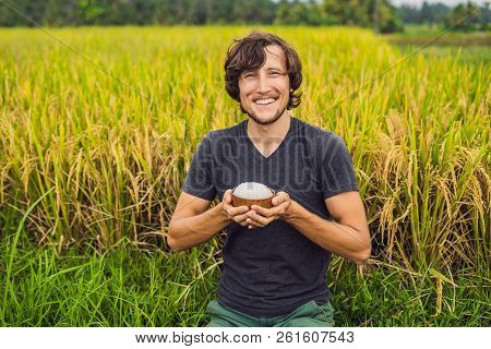 Man Is Holding A Cup Of Boiled Rice In A Wooden Cup On The Background Of A Ripe Rice Field