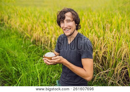 Man Is Holding A Cup Of Boiled Rice In A Wooden Cup On The Background Of A Ripe Rice Field