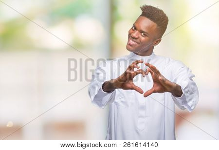 Young arabic african man wearing traditional djellaba over isolated background smiling in love showing heart symbol and shape with hands. Romantic concept.