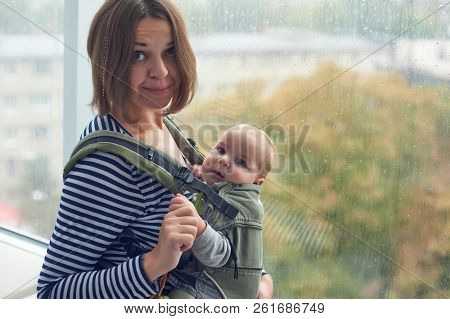 Mother With Ergobaby Carrying Toddler At Home.